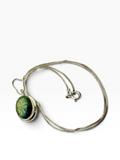 A silver chain necklace with a round pendant featuring a green and black starburst pattern, displayed on a clean white background.