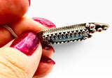 A close-up of a hand holding a silver-handmade pendant with a dark blue-green labradorite rectangular stone 