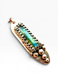 A textured silver pendant featuring a central iridescent  labradorite blue-green stone inlay, surrounded by a decorative border of small metallic loops and a cluster of raised round beads on one end, shown on a plain light gray background.