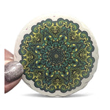 Round decorative item with green and black mandala pattern on a white background