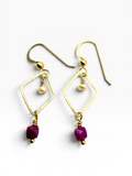 A pair of gold dangle earrings with geometric diamond-shaped wire frames, small gold beads, and faceted purple gemstone drops, shown on a clean white background.