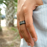 Hand wearing a black and silver checkered ring with a blurred natural background