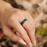 Hand wearing a blue ring with a blurred natural background