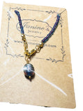 Necklace with blue beads and a large blue and gold pendant on a Jamine's Jewelry card.