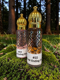 Two ornate glass perfume bottles with gold caps and white labels reading '#22 Ever Ending story' placed on green moss outdoors with trees in the background.
