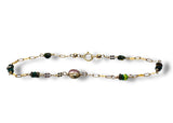Gold chain bracelet with green and purple beads on a white background