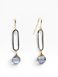A pair of gold and black paperclip dangle earrings with a faceted light blue-gray gemstone hanging from each.