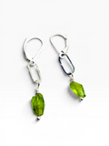 A pair of silver drop earrings with faceted green gemstone pendants, displayed on a clean white background.