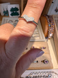 A silver ring with a heart-shaped cluster of clear crystals worn on a finger, shown in a jewelry display setting.