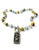A beaded necklace with a silver-toned toggle clasp and a rectangular paw print pendant. The beads are made of marbled stone in various colors including light blue, olive green, brown, and cream, strung on silver links.