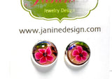 Pair of earrings with pink floral design on a white background, featuring Janine Jewelry Design branding.