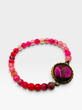 A beaded bracelet featuring vibrant pink, red, and orange translucent beads, with a prominent round gold-toned medallion containing a pink floral inlay, displayed on a clean white background.