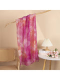 Pink and orange tie-dye scarf hanging on a wooden stick against a beige wall.