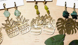 Gold plant-themed earrings on a wooden surface with green leaves.