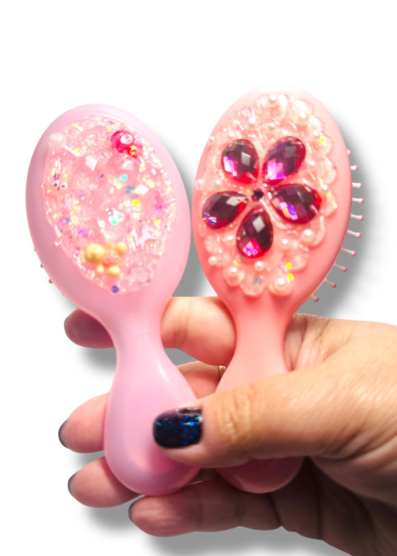 Pink baby brush with decorative elements held by a hand on a white background