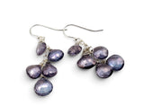 A pair of handmade dangle earrings featuring faceted, irregular purple gemstones wrapped in silver wire and suspended from silver fishhook wires, shown on a plain white background.