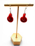Red earrings on a gold earring stand against a white background