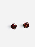 A pair of round stud earrings featuring deep red gemstones in a four-prong setting, shown against a plain light gray background.