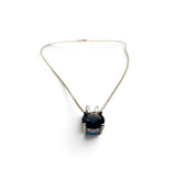 A delicate gold chain necklace with a central pendant featuring a large, faceted dark blue gemstone held in a silver-toned prong setting, shown on a clean white background.