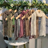 Scarf display with various patterns on a wooden rack against a white wall.