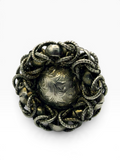 An ornate vintage silver-toned brooch featuring a central engraved oval medallion surrounded by a textured circular border of twisted rope-like links and small dome accents, shown on a plain white background.
