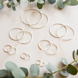 Silver hoop earrings on a light surface with green leaves