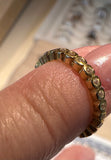 A close-up of a gold eternity ring with small clear stones set in a scalloped band, worn on a finger.