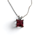 A silver-toned necklace with a square princess-cut dark red gemstone pendant, shown on a clean white background.