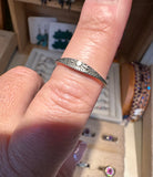 A silver ring with a sunburst engraved pattern and a small central white stone, shown worn on a finger in a jewelry display setting.