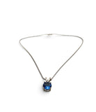A delicate silver chain necklace featuring a small bezel-set oval blue gemstone pendant, displayed against a clean white background.