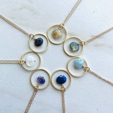 Gold necklaces with circular pendants featuring various stones on a light background