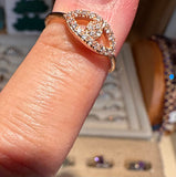 A close-up of a rose gold ring with a diamond pavé eye design worn on a finger, with a jewelry display case blurred in the background.