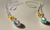 Two necklaces with beaded chains and colorful beads on a neutral background