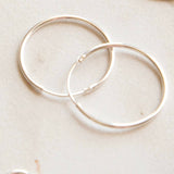 Two silver hoop earrings on a light beige surface