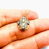 A small gold pendant necklace with a floral design, held on a person's fingers against a plain white background.