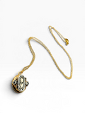 A gold chain necklace with an oval locket pendant featuring a floral design, photographed on a clean white background.