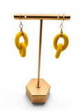 Yellow earrings on a gold earring stand against a white background