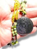 Necklace with green beads and a large decorative pendant held in a hand against a white background