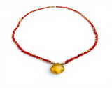 Necklace with red beads and a yellow pendant on a white background