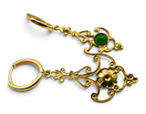 A pair of gold leverback earrings with ornate filigree scrollwork, a flower motif, and a round green cabochon gemstone, shown on a white background.