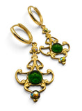 A pair of gold hoop earrings with ornate filigree details, featuring round green cabochon gemstones and small iridescent rhinestones, shown on a white background.