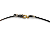 Close-up of a black cord bracelet or necklace with a gold-filled clasp and wrapped metal details on a white background.