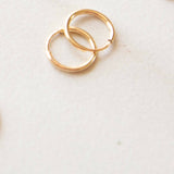 Two gold hoop earrings on a light beige background