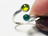 Silver ring with green gemstone held by a finger against a white background