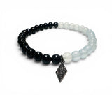 Beaded bracelet with black and white beads and a decorative charm on a white background
