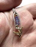 Gold hummingbird pendant with blue iolite beads on a silver chain held between fingers.