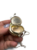 Hand holding a silver locket with an open shell design on a white background