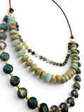 A multi-strand beaded necklace featuring dark green faceted forest jasper stone beads, light ocean jasper beads, bloodstone coin beads separated by small gold spacer beads, suspended on leather cord against a white background.