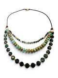 A multi-strand beaded necklace featuring dark green faceted forest jasper stone beads, light ocean jasper beads, bloodstone coin beads separated by small gold spacer beads, suspended on leather cord against a white background.