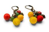 A pair of dangling earrings with translucent red, yellow, and green glass beads attached to antique bronze leverback hooks, shown on a white background.